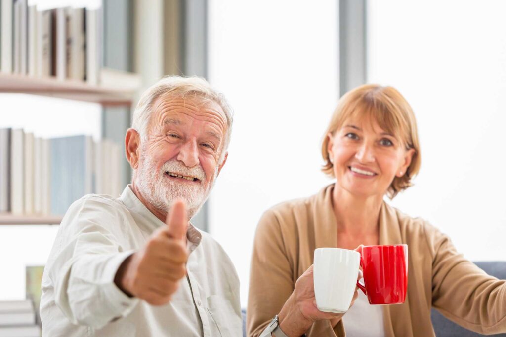 Smiling elderly couple showing thumbs up with holding cups of coffee