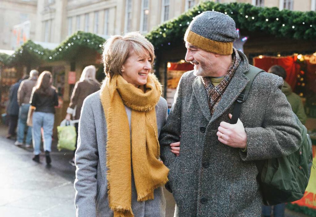 A mature married couple are walking through a Christmas market together.