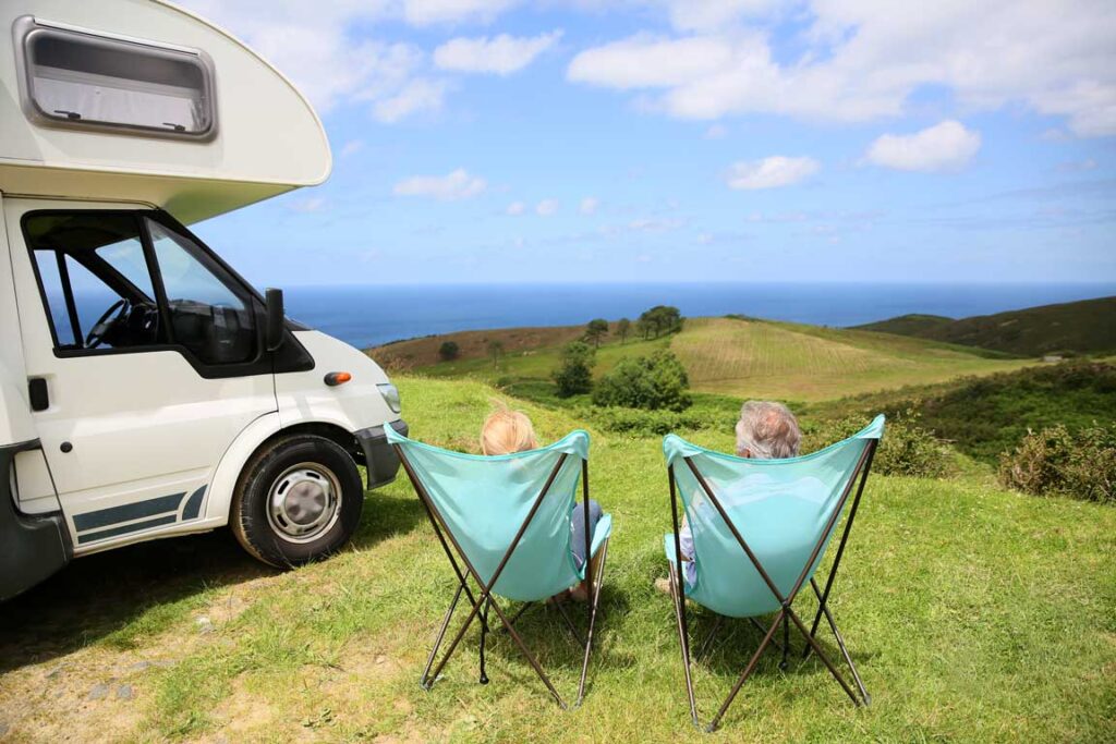 Senior couple relaxing in camping folding chairs beside motorhome